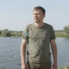 A 35-year-old man standing near a pond in Mordovia, wearing casual clothing, looking concerned or searching, with natural landscape and water details, no text or symbols