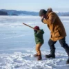 A man in winter clothing violently striking an eight-year-old boy with a stick on a frozen lake surface, both figures centered on the ice, cold atmosphere, realistic winter landscape with snow-covered surroundings and distant mountains, no text or symbols on the ice