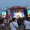 A vibrant outdoor music festival in Chelyabinsk featuring a large stage with colorful lights, a diverse crowd of people dancing and cheering, prominent Russian celebrities performing on stage, festive decorations, and a lively atmosphere under a clear evening sky