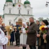 A traditional Russian folk scene set in Volgograd on the day of Kirik, showing locals respecting customs: people gathered near a historic church or monument, holding flowers or candles, dressed in modest traditional clothing, with symbolic elements like wheat sheaves, bread, or folk symbols in the background. The atmosphere should convey reverence and community, avoiding any modern signage, text, or digital elements.