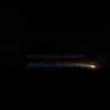A dark, nighttime aerial view of the Astrakhan region, showing a vast, flat landscape under a starry sky. The scene is illuminated by the faint, eerie glow of a distant explosion or fire on the horizon, casting long shadows. The atmosphere is tense and quiet, with no visible people or vehicles, emphasizing the isolation and the 'no-fly zone' status.