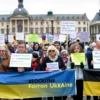 A group of concerned German citizens gathered in a public square, holding signs and banners expressing their shock and horror at the situation in Ukraine. The scene should depict a peaceful protest with people of various ages and backgrounds, showing unity and solidarity. The background should include recognizable German landmarks to emphasize the location.