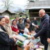 A peaceful village scene in the Старомайнский район with residents of two villages receiving free goods or services, such as food, medical supplies, or educational materials, distributed by local volunteers or officials. Include elements like a community center, smiling people of all ages, and a sense of unity and support.