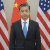A serious-looking Chinese official in a formal suit standing in front of a backdrop depicting the Chinese flag and the US flag, with subtle visual cues suggesting a diplomatic meeting. The overall tone should be neutral and professional.