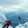 A dramatic scene depicting two alpinists falling from the steep, snow-covered slopes of Mount Elbrus, with a vast mountainous landscape in the background under a cloudy sky, conveying the tragedy of their accident