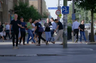 A bustling city street with people walking and interacting, focusing on a section where broken or damaged tiles are visible on the pavement. Show a realistic urban environment with pedestrians, some looking at the damaged tiles, others walking past. Include elements like street signs, trees, and vehicles in the background to emphasize the city setting.