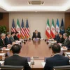 A serious diplomatic meeting in a large conference room with officials from the United States and Iran. The room is filled with people sitting around a long table, engaged in intense discussions. The atmosphere is formal and tense, with flags of both countries displayed prominently. The lighting is professional and bright, highlighting the seriousness of the event.