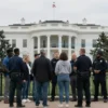 A tense scene of a group of people standing near the White House, surrounded by police officers and security, with a subtle sense of tension and suspicion. The Washington, D.C. skyline and the White House are visible in the background. No text, letters, digits, or logos should appear in the image.