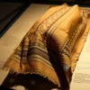 A mysterious ancient silk fabric with intricate woven patterns, believed to be the type used in the famous 'Chelyabinsk silk' artifact, displayed under soft museum lighting with a subtle metallic sheen, surrounded by faint archaeological context like aged parchment and dust particles