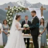 A beautiful wedding ceremony taking place outdoors in Vladikavkaz, with the Caucasus Mountains in the background. The bride and groom are exchanging vows, surrounded by guests. Traditional Caucasian clothing is visible. The scene should convey joy and celebration, highlighting the region's beauty.