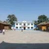 A small rural village with traditional wooden houses, a central square with a small clinic or medical building, people going about their daily activities, a clear blue sky, and a sense of community and tranquility.