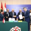 A formal event scene with representatives from different countries or organizations shaking hands and signing documents on a table. The background should include flags of participating nations and a banner with the INNOPROM logo. The atmosphere should be professional and celebratory, with people dressed in business attire.