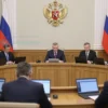 A serious and professional setting inside the Russian State Duma, with members of the parliament engaged in a discussion. The scene should include a large conference table with documents and laptops, a podium with a microphone, and a backdrop featuring the emblem of the State Duma. The atmosphere should convey the importance and gravity of the discussion about military contracts.