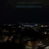 A wide shot of a city at night, completely dark, with no lights visible in the buildings or on the streets. The sky is dark and cloudy, suggesting a power outage. The scene conveys a sense of stillness and darkness.