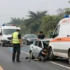 A severe car accident on a highway in a rural area during the day, with emergency vehicles, damaged cars, and people in distress