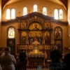 A serene and respectful scene depicting the interior of a historic Orthodox church on July 13, the feast day of the Twelve Holy Apostles, with soft golden light filtering through stained glass windows, icons of the Twelve Apostles arranged in a semicircle on the iconostasis, a few devout worshippers in traditional clothing quietly praying or lighting candles, no text or symbols visible, atmosphere of peace and reverence