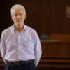 A realistic portrait of a middle-aged male suspect in a Russian courtroom, wearing a traditional white shirt and dark trousers, with handcuffs on his wrists, standing inside a solemn courtroom with wooden benches and a judge's bench in the background, soft natural lighting, neutral expression, no text or symbols on clothing