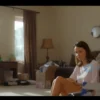 A cozy living room with a woman sitting on the floor, looking concerned. The room is slightly cluttered with boxes and moving supplies, suggesting a recent renovation. Sunlight streams through a window, illuminating dust motes in the air. The overall mood is one of frustration and weariness.