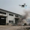 A damaged warehouse with debris, smoke, and a destroyed drone in the sky, showing the aftermath of an attack on a storage facility