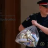 A police officer in uniform is escorting a bag containing packages of drugs into the courthouse in Stavropol. The scene should depict law enforcement activity and the seriousness of the situation. Focus on the officer and the bag of evidence.
