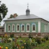A historical scene depicting a 19th-century house in Tula, Russia, with a focus on the architectural details of the era. The house should be surrounded by a lush garden with traditional Russian flowers and trees. In the background, there should be a hint of municipal buildings, suggesting the context of the story. The image should convey a sense of nostalgia and historical significance.