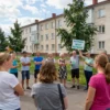 A group of people in a residential area of Arkhangelsk, Russia, gathered in a discussion. They are standing outside their homes, some holding signs or posters with messages about energy conservation. The background shows typical Russian apartment buildings and a few trees. The scene is set during a warm summer day, with people wearing casual summer clothing.