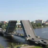 A wide-angle, high-resolution photograph of the Imperial Bridge in Ulyanovsk, Russia, showing the bridge fully open to traffic. The image should capture the bridge's distinctive arch design, the flow of vehicles on the roadway, and the surrounding river and cityscape under clear daylight conditions. The perspective should be from a slightly elevated viewpoint to showcase the bridge's structure and its integration into the urban environment.