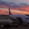 A commercial airplane on a tarmac at an airport in the USA with a large fuel truck nearby, dramatic sky suggesting economic pressure, realistic lighting, no text or logos