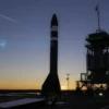 A sleek modern reusable rocket standing on a launch pad at sunrise, with the Japanese flag subtly visible in the background, detailed metallic textures, realistic lighting, and a sense of technological advancement