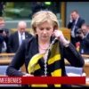 A female Member of the European Parliament standing in a formal legislative chamber, holding a flag with a black and yellow design, in the act of tearing the fabric apart with both hands. The scene is captured in a dramatic, high-definition news broadcast style, with blurred background showing other officials and cameras, emphasizing the intensity of the moment without any visible text or logos.