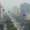 A microscopic view of ultrafine particles in the air, depicted as tiny, colorful dots floating in a hazy atmosphere. The background should show a cityscape with buildings and vehicles to emphasize the urban environment where these particles are prevalent. The image should convey a sense of pollution and its impact on health.