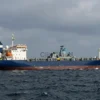 A large cargo ship sailing in the Black Sea, with a Ukrainian warship in the background. The sky is overcast and dramatic, suggesting a tense situation. Focus on the ships and the sea.