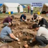 A vibrant outdoor scene in Stavropol, Russia, showing a group of archaeologists conducting an excavation at a historical site. The image should depict people carefully brushing soil, uncovering ancient artifacts like pottery shards and tools, with tents, equipment, and a banner reading 'XIV Неделя археологии' in the background. Include a mix of adults and students, diverse attire, and a sunny day with clear skies. The atmosphere should be lively and educational, with attention to realistic detai