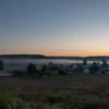A serene pre-dawn scene in a rural area of Voronezh region, Russia. Soft morning light illuminates the landscape, with fields, forests, and small villages in the background. A sense of calm and relief is conveyed as the threat has passed. The sky is transitioning from dark to light, with a few stars still visible.