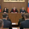 A courtroom scene in Russia showing a formal legal proceeding with judges in robes, lawyers in suits, and officials from the Russian Ministry of Defense seated at a table, with a prominent sign or document displaying 'ПАО «Завод Тула»' in the background, realistic lighting and detailed textures