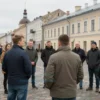 A street meeting in Smolensk city center with a local official speaking to a small group of people on a cobblestone street, historic buildings visible in the background, natural daylight, realistic human figures, no text or signs