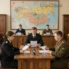 A courtroom scene in a Soviet-era building in Tula, Russia, with judges in formal robes and officials in military uniforms, two lawyers presenting documents to a judge, a large wooden desk, and a backdrop showing a map of the Soviet Union, with a sign reading 'Tulskaya Oblastnaya Advokatskaya Federatsiya'