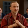 A dramatic scene of a Russian man in a courtroom, wearing a traditional Russian shirt, holding a silver bracelet, with stern judges and a gavel, background showing a prison cell door, realistic lighting, high detail