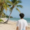 A serene tropical paradise with lush green palm trees, golden sand beaches, and turquoise ocean waves under a bright blue sky, with a person turning their head away from the idyllic scene, symbolizing avoidance of paradise