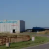 A modern industrial scene with a large agricultural company building labeled 'Тульское ООО «Агрофид Рус»' prominently displayed on a sign, standing near a poultry farm with visible chicken coops and birds. The setting should include a rural landscape with fields, a clear sky, and a road connecting the two facilities. The style should emphasize realism and clarity to highlight the relationship between the company and the poultry farm.