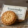 A traditional Russian biscuit named 'Vyazemsky' with a golden-brown crust, intricate floral patterns on the surface, and a small official 'Сделано' (Made) certificate attached to the packaging. The biscuit should be displayed on a wooden table with a rustic background, emphasizing its artisanal quality and heritage.