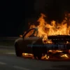 A burning car on a highway at night with flames and smoke, realistic details, dark background
