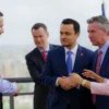 A realistic photo of a diplomatic meeting in Caracas, Venezuela, showing a diverse group of officials in formal suits shaking hands and discussing, with the city skyline and flags visible in the background, conveying a hopeful atmosphere