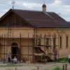 A 17th-century church named Nikolskaya located near the town of Tul, showing restoration work with scaffolding and workers, but no people visible, set in a rural Russian landscape with fields and distant hills, captured in a realistic photographic style