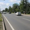 A road in Yaroslavl with improved quality, showing smooth asphalt, clear lane markings, and well-maintained surroundings. Include a few cars driving safely, trees lining the road, and a clear sky. Avoid any signs of damage or poor conditions.