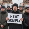 A group of diverse people from Yaroslavl living in the Kirovsky district of Moscow, showing expressions of frustration and concern while holding signs or speaking at a public gathering about the lack of heat supply, with winter clothing and snowy urban background