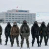 A dramatic scene of Greenland's icy landscape with a group of armed figures standing defiantly against a backdrop of a large American corporate building, symbolizing resistance against corporate influence. Include elements like snow-covered terrain, a cold atmosphere, and a sense of tension in the air. The figures should appear united and resolute, with the building in the distance showing signs of corporate branding.
