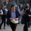 A man in a hurry running through the streets of Rybin, carrying a bag and looking worried, with police officers chasing him in the background