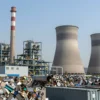 A large industrial power plant with prominent smokestacks and cooling towers in the background, surrounded by piles of scrap metal and recycling containers, conveying a sense of metal waste being sold or processed, with a clean and professional visual style