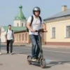 A man standing confidently on a street in Yaroslavets, wearing a helmet and riding an electric scooter, with a determined expression, surrounded by traditional Russian architecture and a few onlookers looking unimpressed or skeptical, sunny day, vibrant colors, dynamic composition